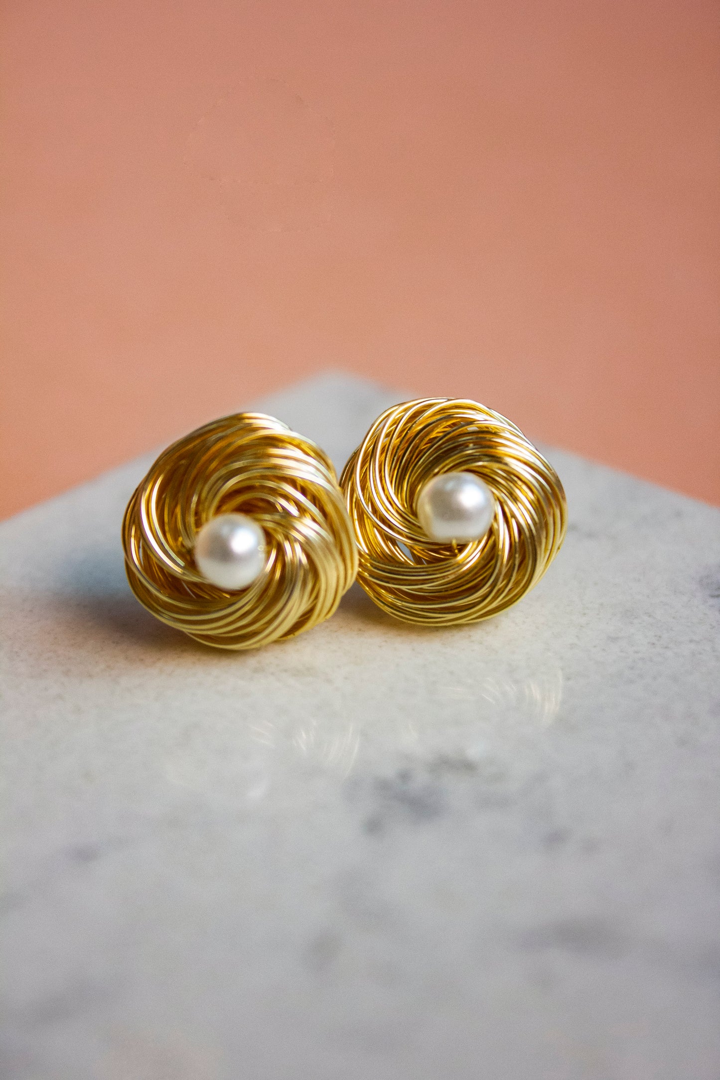 Gold knotted earrings with pearl centers on a marble surface
Jewelry photography