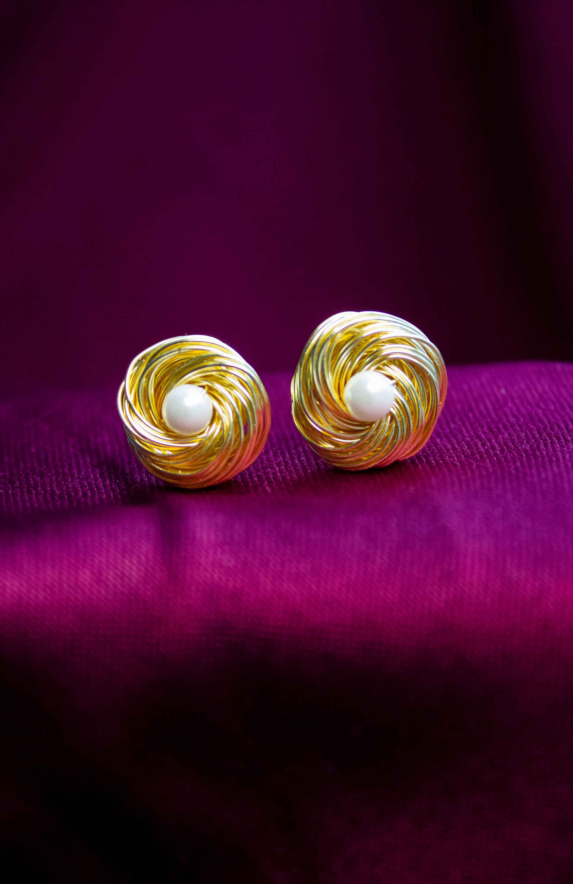 Gold spiral earrings with pearl centers on a purple background